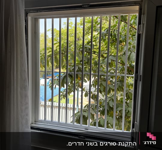 חלון עם סורגים מול נוף עצים ירוקים